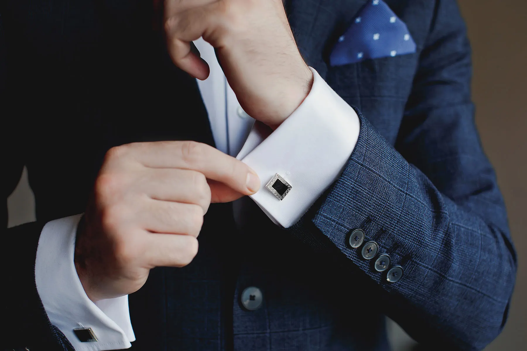 A square cufflink fastened on a French cuff under a navy suit jacket