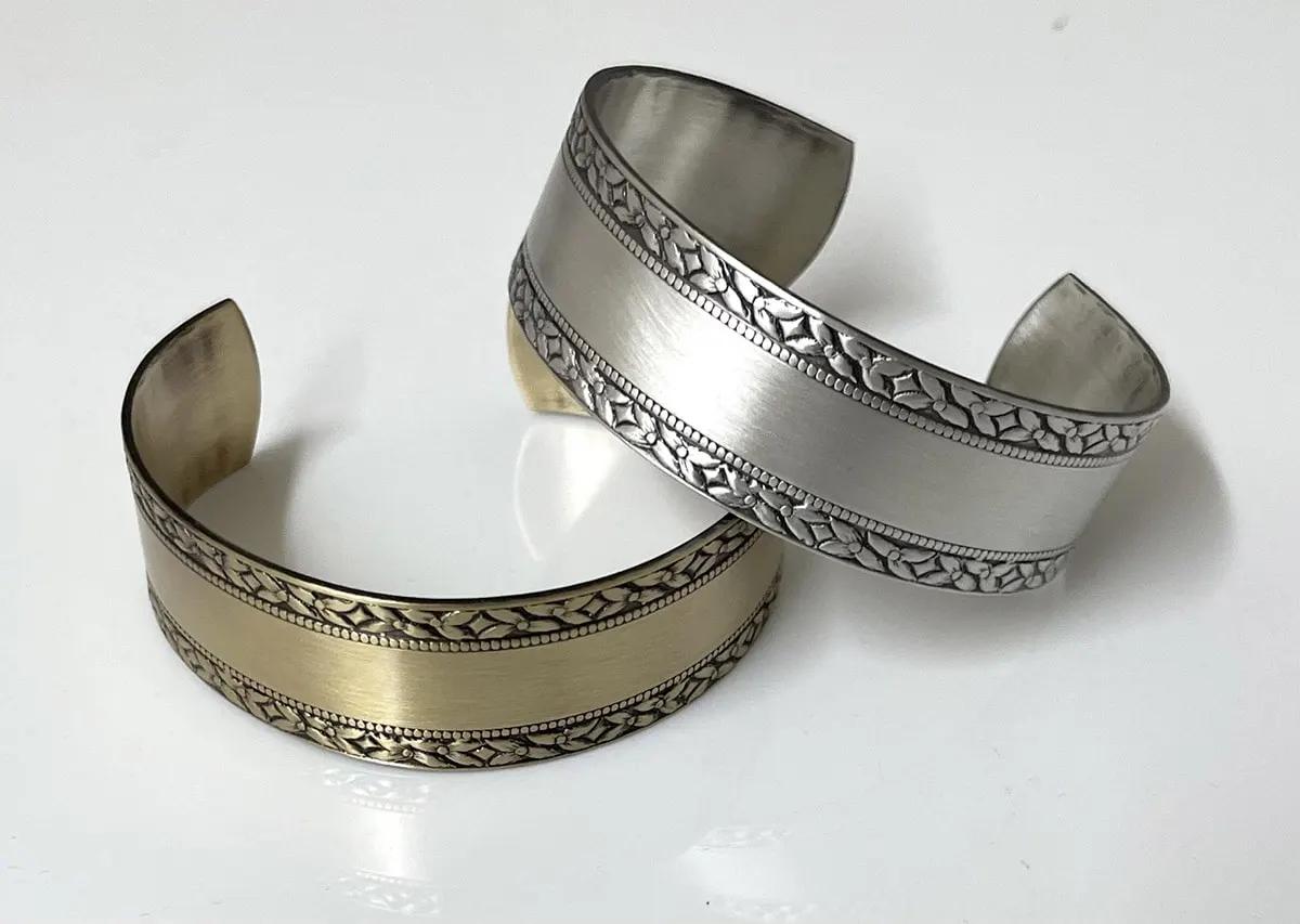Two embossed cuff bracelets, one in antique brass and one in satin silver