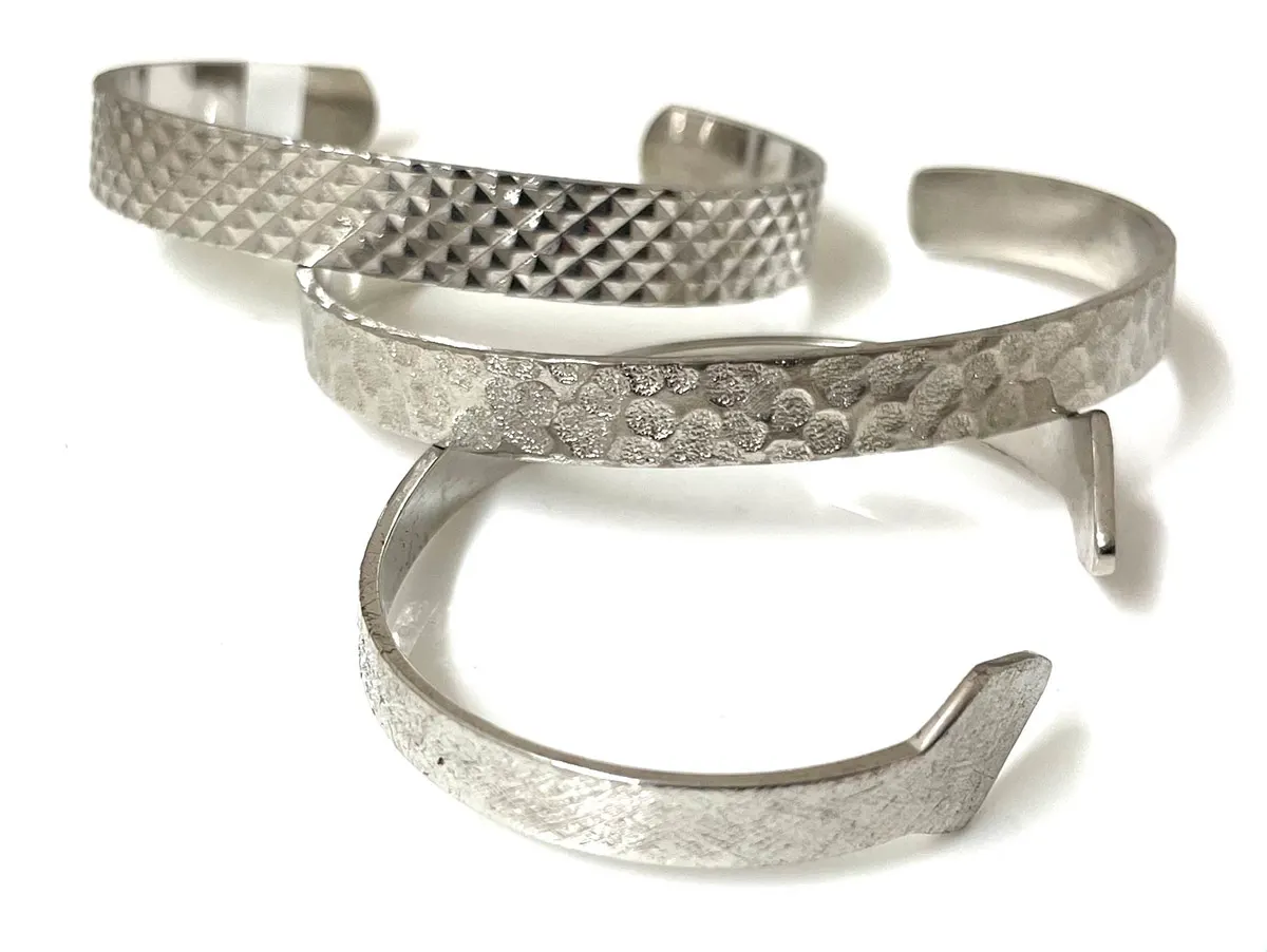 Three stamped cuff bracelets with textured and hammered patterns in a silver finish