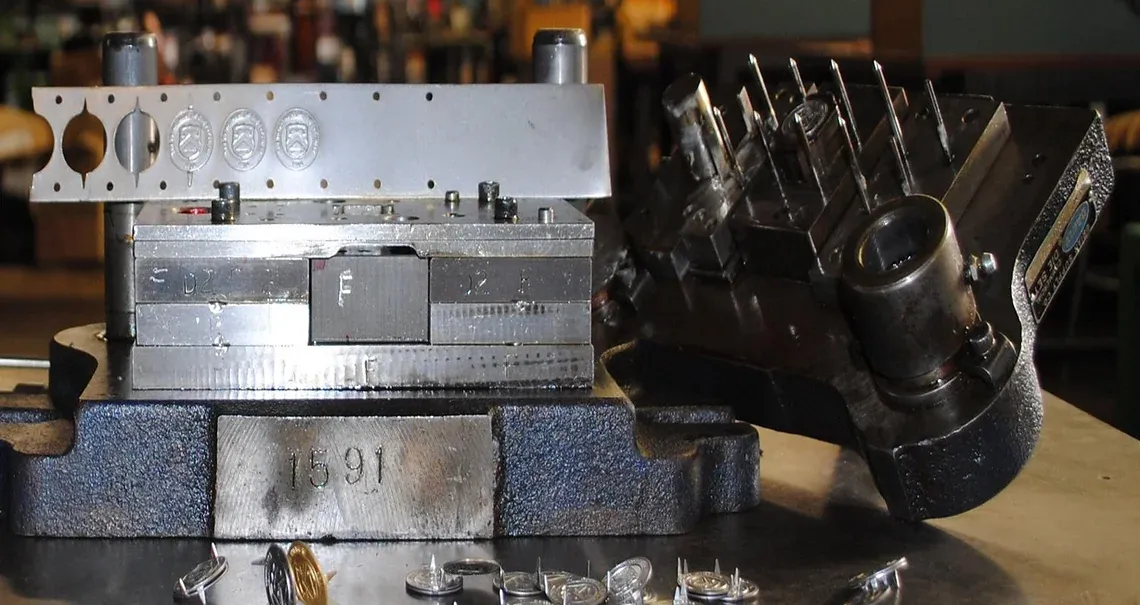 A stamping die set clamped on the bench, with freshly stamped parts below it