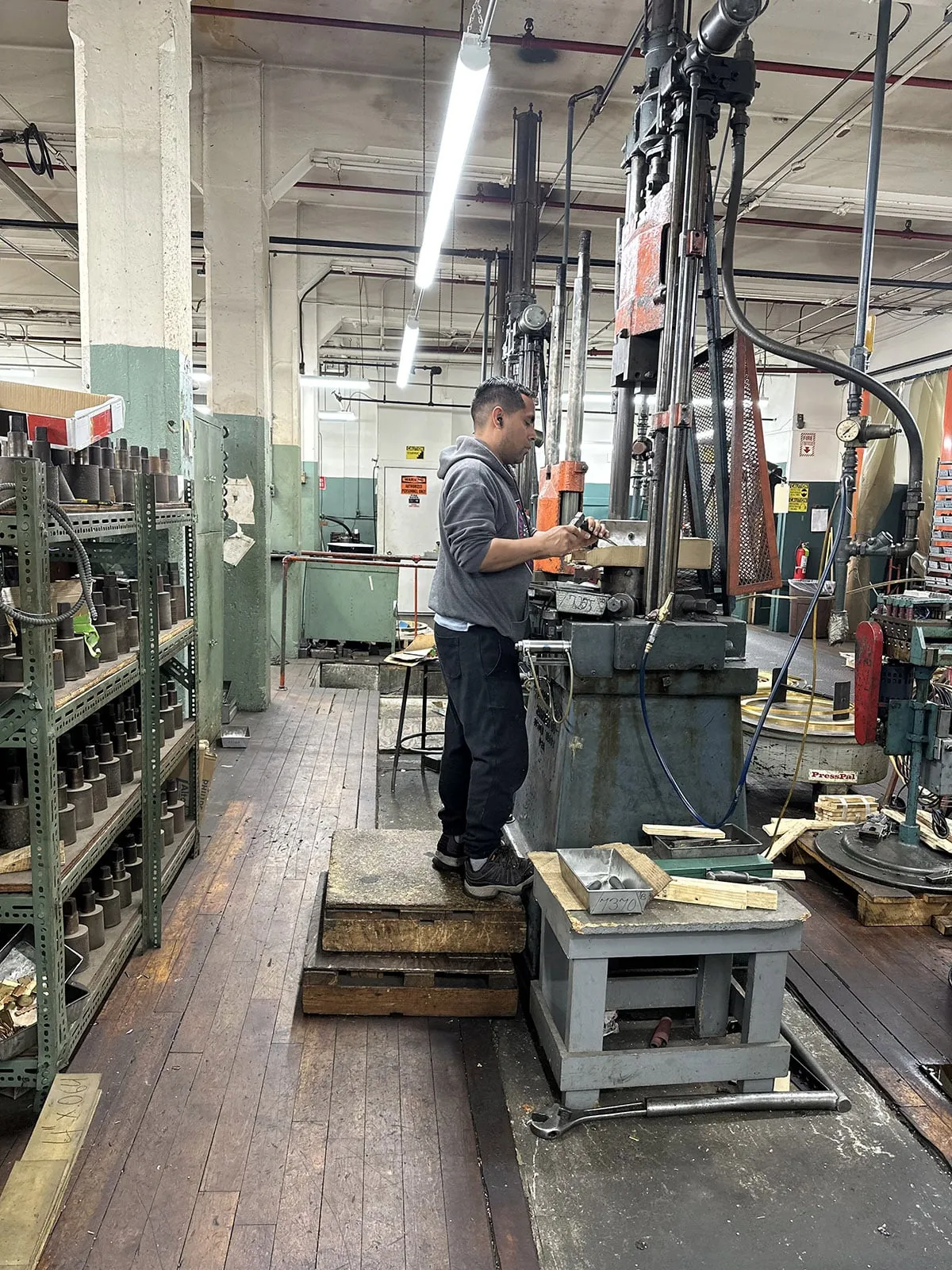 An operator at a stamping press in an aisle lined with tooling shelves