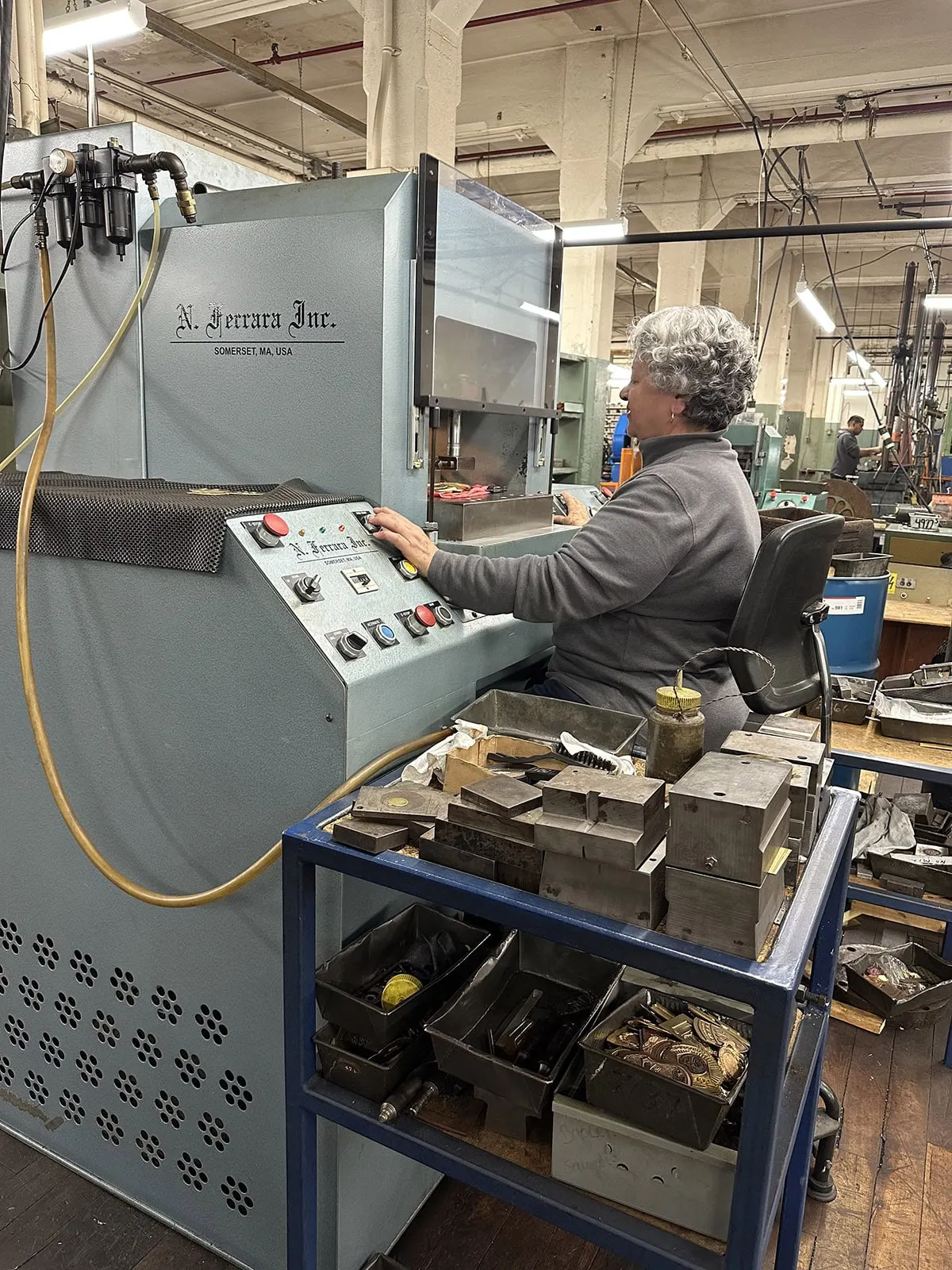 An operator at the control panel of a stamping press, beside a cart of dies